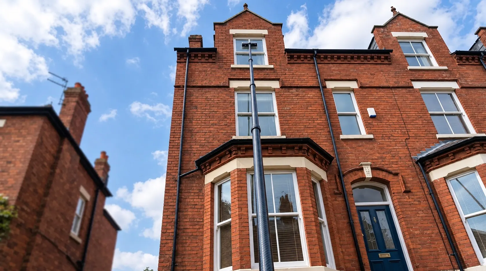 Water-fed pole window cleaning reaching the top-floor windows of a three-storey red-brick townhouse