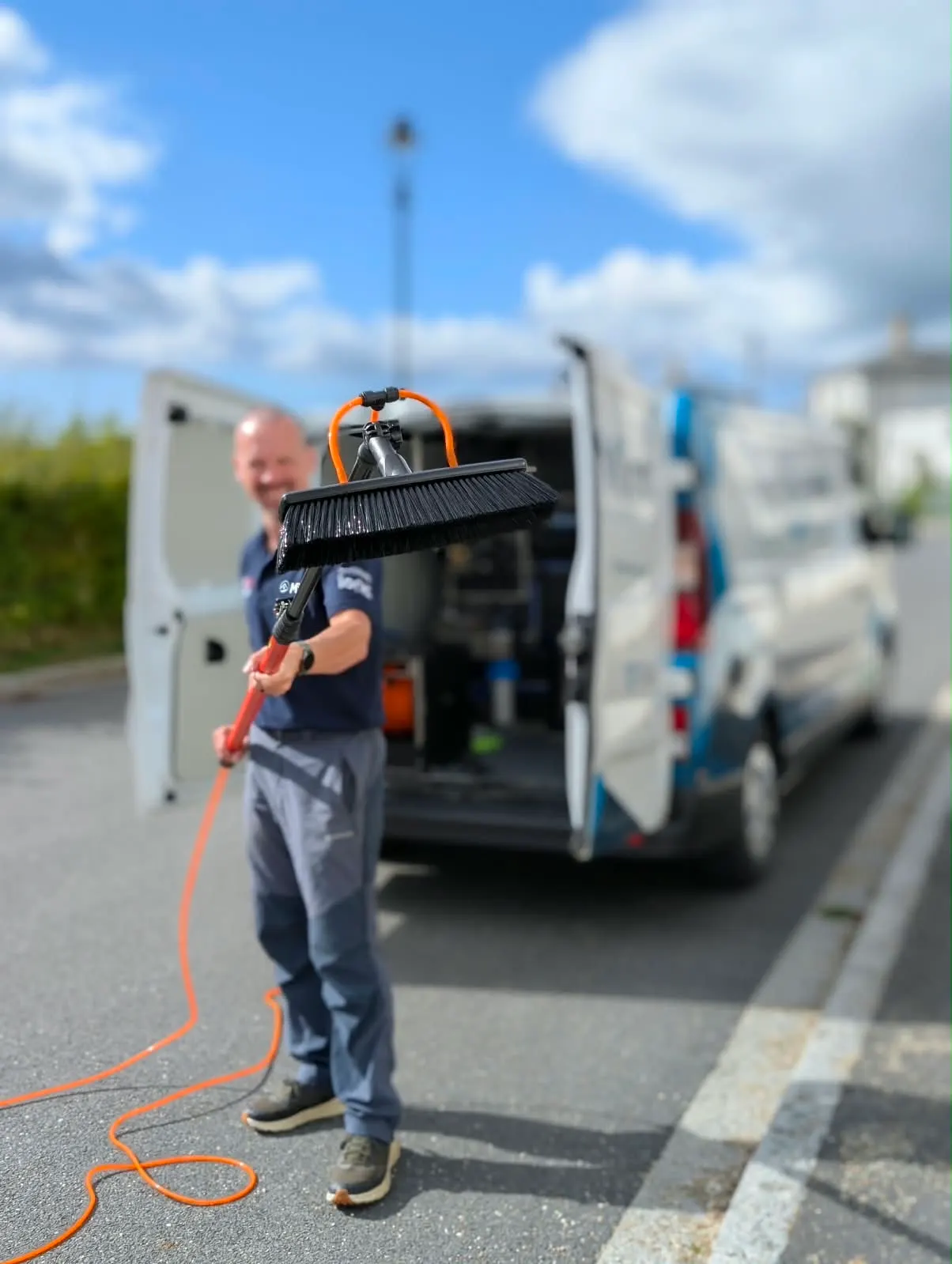 Tom from Mint holding a water fed pole brush in front of the Mint window cleaning van